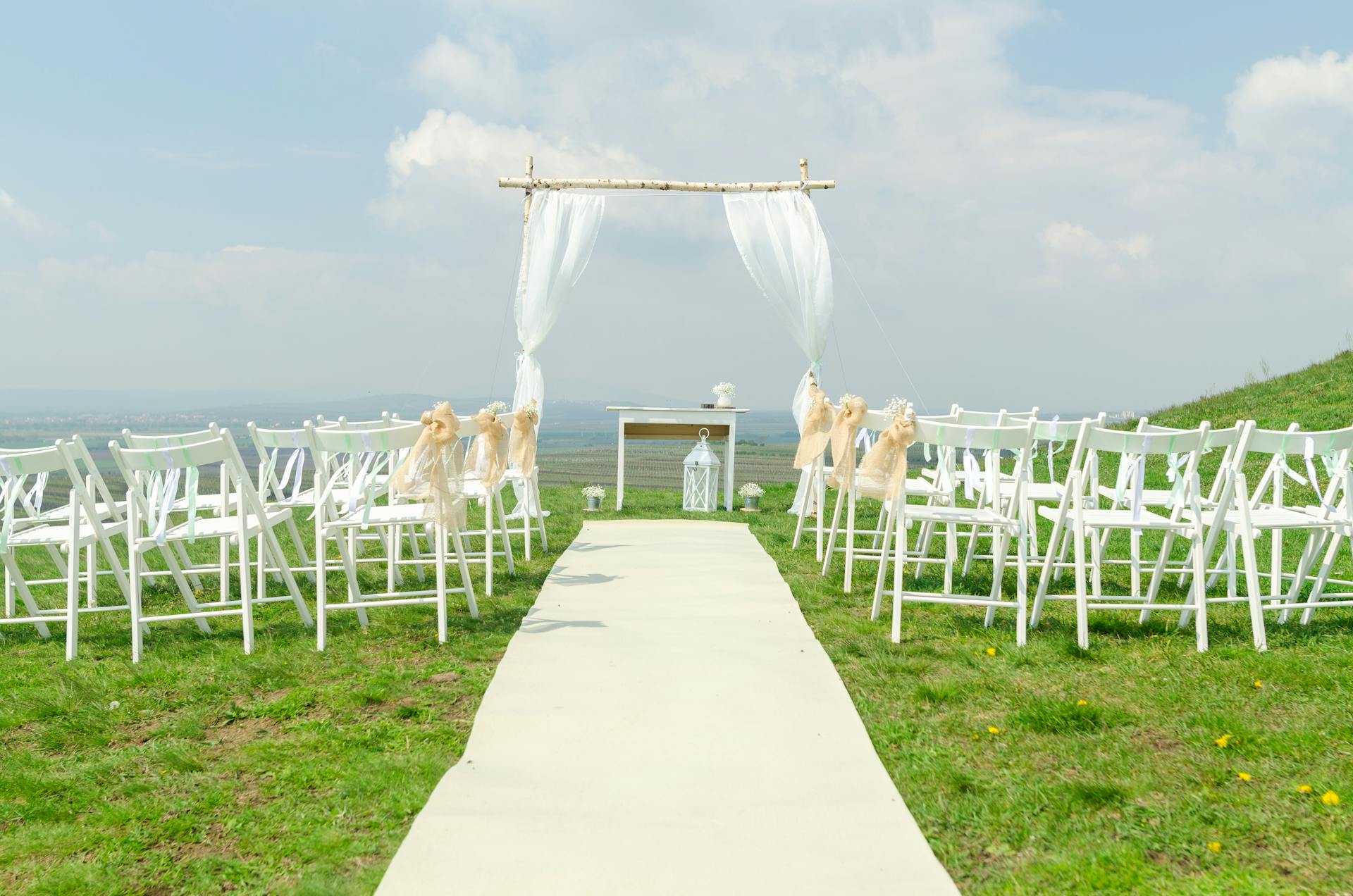 An outdoor wedding venue featuring white guest chairs and an intimate arch for the bride and groom.